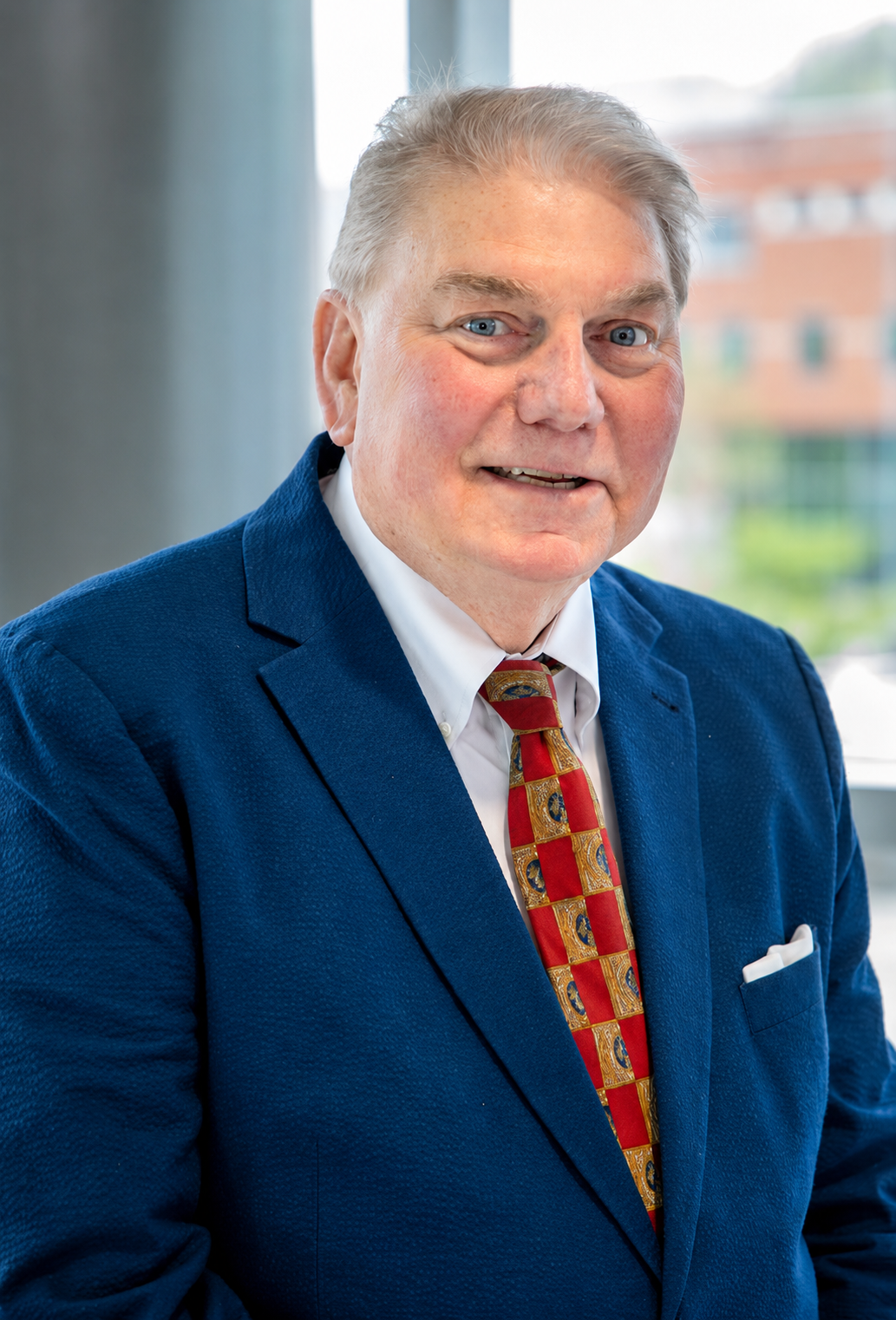A portrait of a man wearing a navy suit and red tie