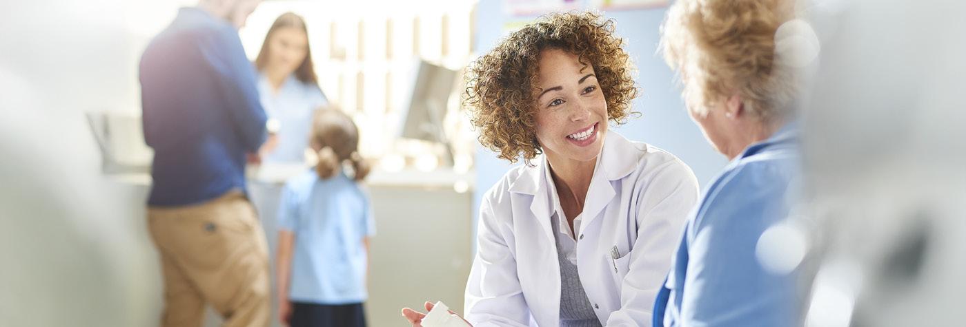 A smiling woman wearing a white coat speaks with a patient.